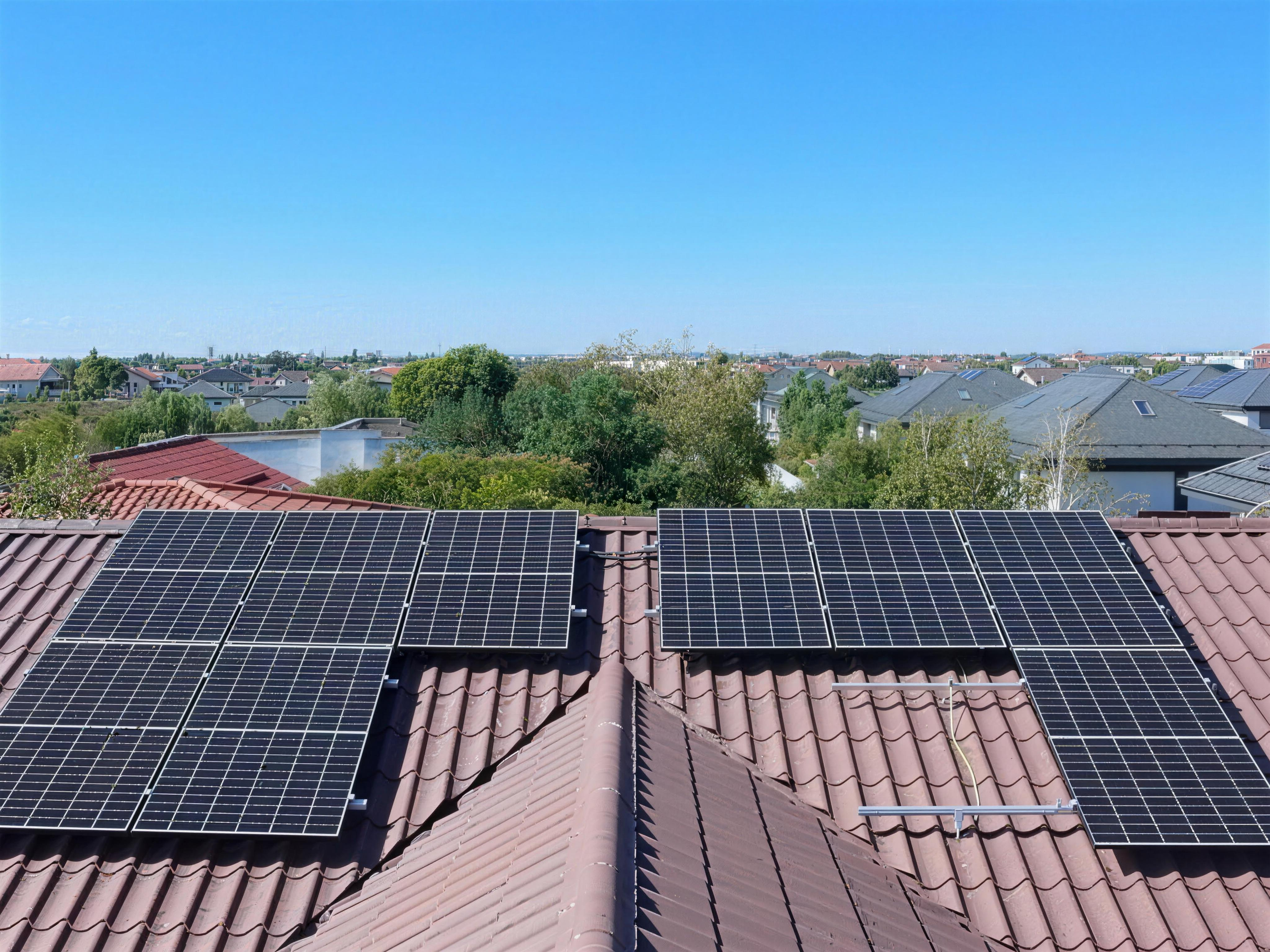 Residential solar panels on a tiled roof overlooking a green suburban neighbourhood